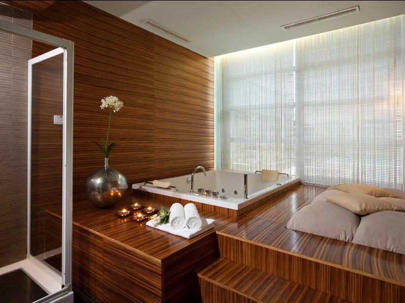 Terrasse mit Steinsitzbank, Kissen und großen Bäumen bei Abenddämmerung unter blauem Himmel.