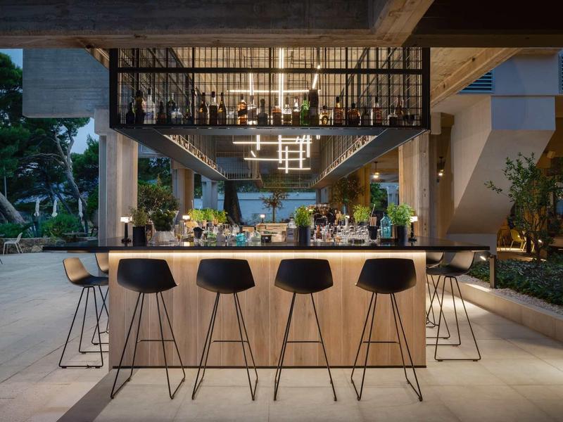 Moderne Outdoor-Bar mit hellem Holz, schwarzen Barhockern und stilvoller Beleuchtung bei Abenddämmerung.