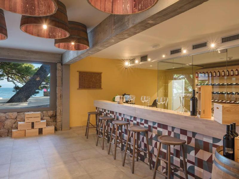 Moderner Barbereich mit Holzstühlen, langer Theke, Weingläsern und großem Fenster mit Baumblick.