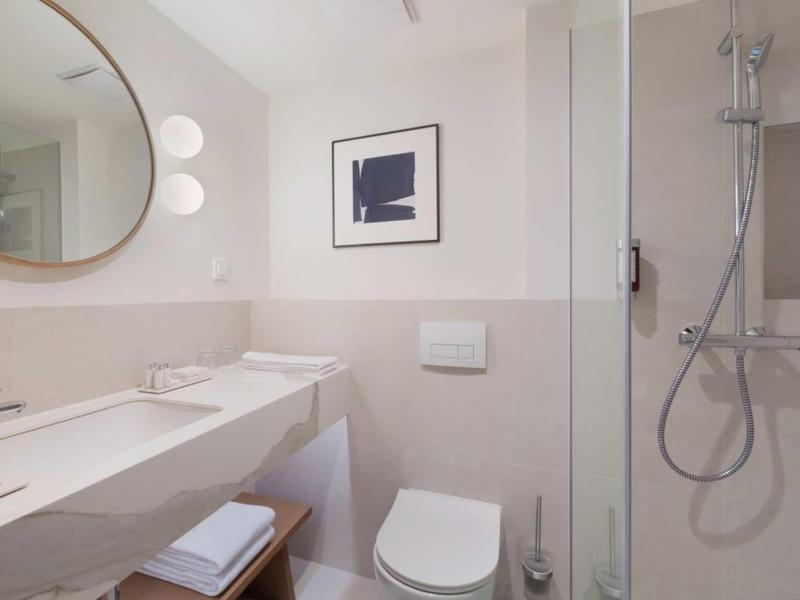 Modernes Badezimmer mit Dusche, Toilette, großem Spiegel und weißen Fliesen.