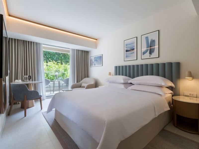 Modernes Hotelzimmer mit Doppelbett, grauem Kopfteil, Schreibtisch, Balkon und neutraler Dekoration.