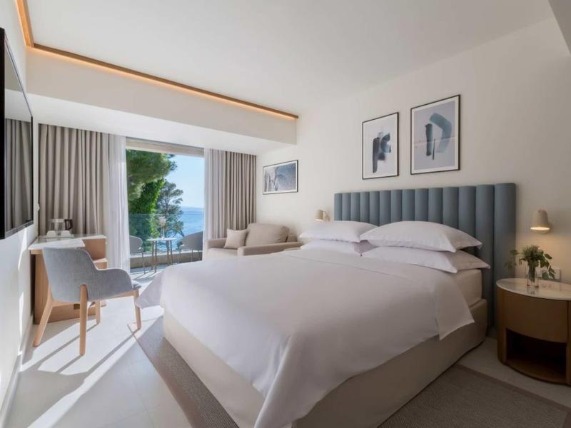 Modernes Schlafzimmer mit großem Bett, grauem Kopfteil, Schreibtisch, Balkon und Blick auf das Meer.