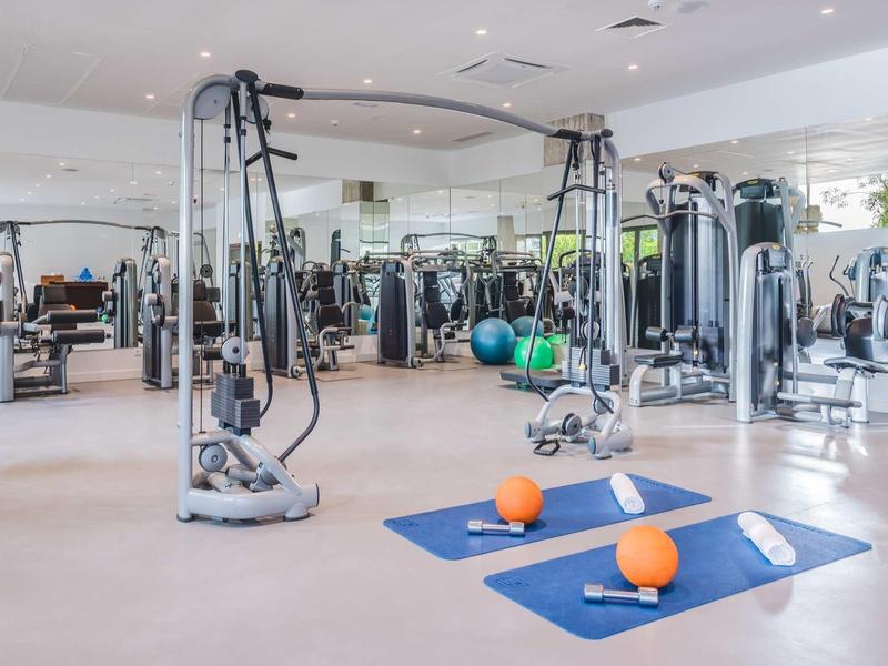 Großer Fitnessraum mit modernen Geräten, Spiegelwänden und Yoga-Matten mit Gewichtsbällen.