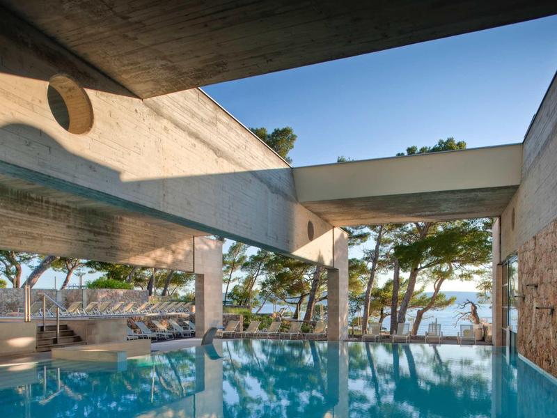 Moderner Innenpool mit klaren blauen Wasser, großem Fenster und Blick auf Bäume und Meer.