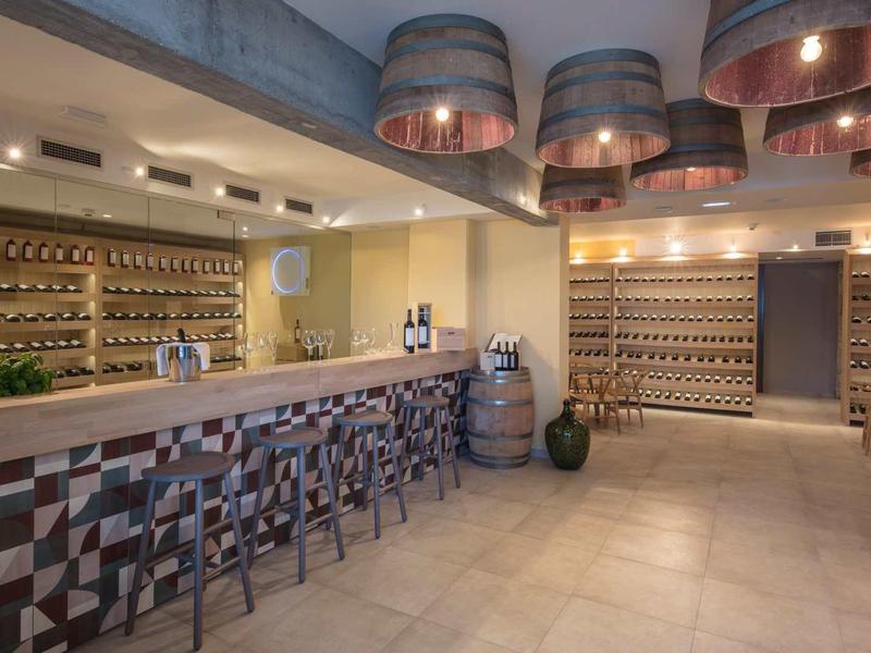 Moderner Weinkeller mit langen Theke, Barhockern, Weinregalen und warmem Beleuchtungskonzept.