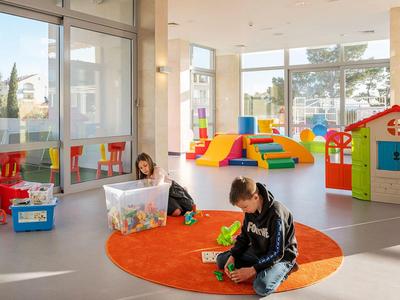 Heller Kindergartenraum mit buntem Spielzeug, Teppich und zwei Kindern, die auf dem Boden spielen.