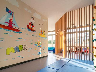 Heller Raum mit bunten Wandbildern und Kletterwand, trennend durch Holzlatten und blauen Bodenmatten.