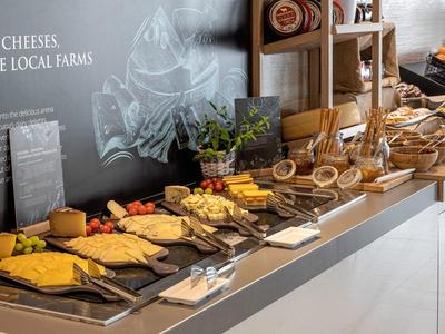 Verschiedene Käsesorten auf Holzplatten, daneben Brot und Kräuter auf einer Buffet-Theke.