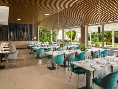 Modernes Hotelrestaurant mit türkisfarbenen Stühlen und großen Fenstern mit Gartenausblick.