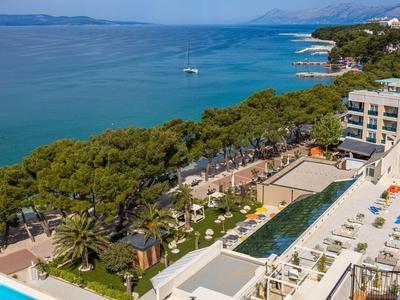 Luxushotel mit Pools und Liegen am Meer, umgeben von grünen Bäumen und blauem Wasser.