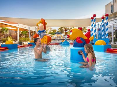 Familie spielt mit bunten Wasserspielzeugen im Pool eines Hotels an einem sonnigen Tag.