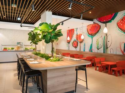 Modernes Restaurant mit hölzernen Tischen, schwarzen Stühlen, roten Bänken und buntem Blumenwandbild.