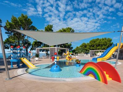 Bunter Kinderspielplatz mit Wasser, Rutschen und Sonnensegel unter blauem Himmel.