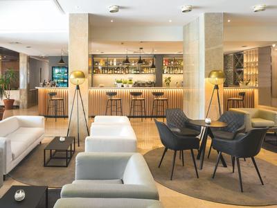 Helles Hotel-Lounge mit weißen Sofas, runden Teppichen und einer Bar im Hintergrund.