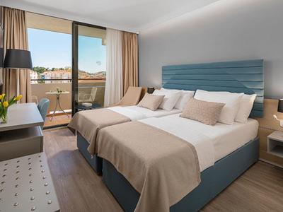 Modernes Hotelzimmer mit zwei Einzelbetten, Balkon und hellen Vorhängen, gemütlich und einladend gestaltet.