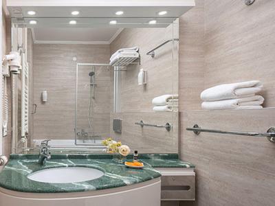 Modernes Badezimmer mit grünem Waschbecken, Spiegel, Handtüchern und Duschkabine in hellem Design.