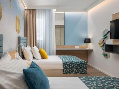 Modern eingerichtetes Hotelzimmer mit zwei Betten, blauen Akzenten und Schreibtisch mit Spiegel.