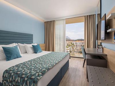 Modernes Hotelzimmer mit großem Bett, blauen Akzenten, Schreibtisch und Balkon mit Stadtblick.