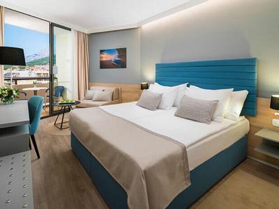 Modernes Hotelzimmer mit großem Bett, blauen Akzenten und einem Fenster mit Ausblick auf Berge.