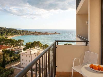 Balkon mit Blick auf das Meer, Holzstuhl, weißer Tisch mit Orangen, bewölkter Himmel.
