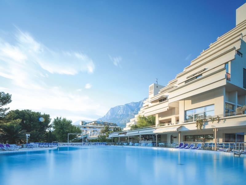 Moderner Hotelpool mit Liegestühlen und Bergblick bei klarem Himmel.