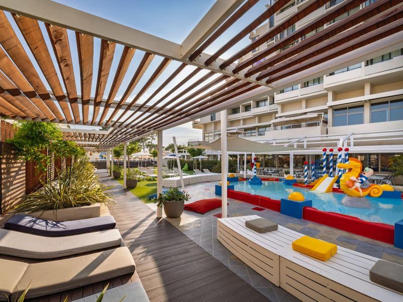 Außenbereich mit Liegestühlen und buntem Kinderpool, modernem Holzdesign und Pflanzen.