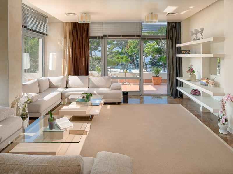 Helles Wohnzimmer mit großer Fensterfront, weißem Ecksofa, Teppichboden und modernen Regalen an der Wand.