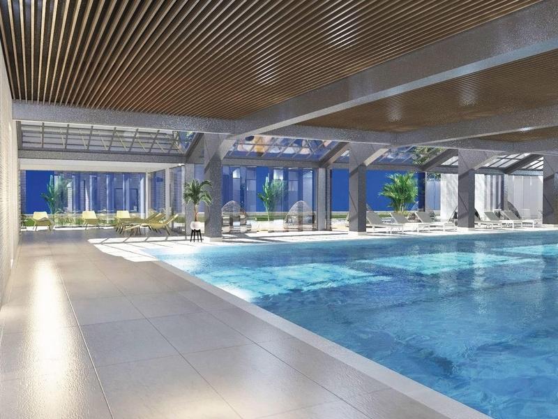 Großer Hallenbadbereich mit blauem Wasser, Glasfenstern und Holzdecke, helle Atmosphäre.