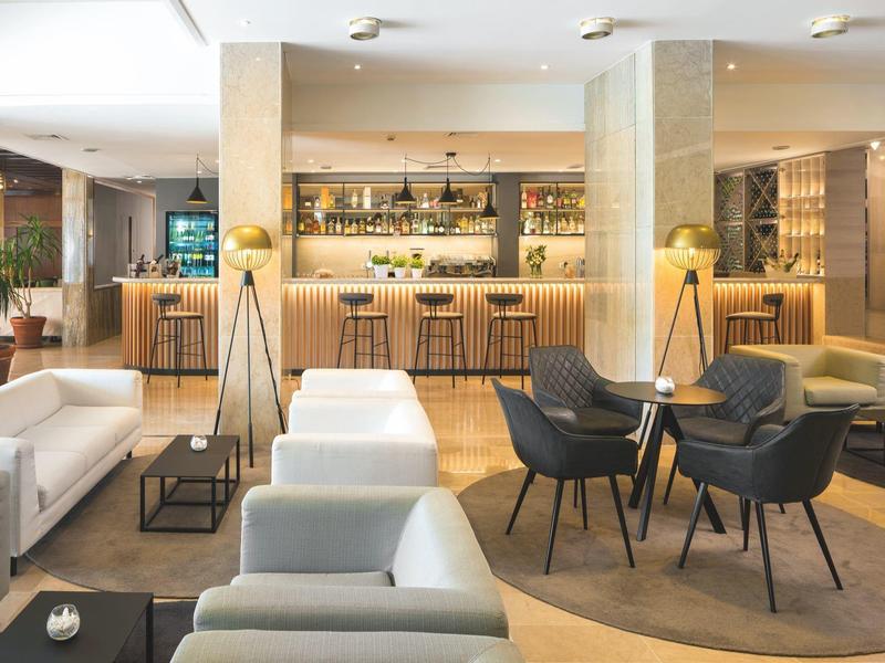 Moderner, heller Lounge-Bereich mit weißen Sofas, schwarzen Stühlen, Stehlampen und gemütlicher Bar.