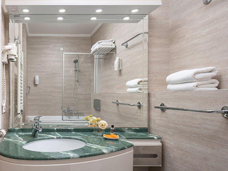 Modernes Badezimmer mit grünem Waschbecken, Spiegel, Handtüchern und Duschkabine in hellem Design.