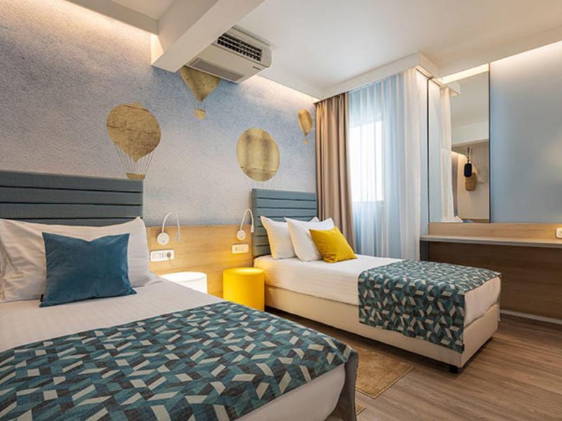 Modernes Schlafzimmer mit zwei Einzelbetten, grauen Kopfstützen, bunten Kissen und Holzboden.