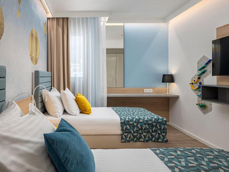 Modern eingerichtetes Hotelzimmer mit zwei Betten, blauen Akzenten und Schreibtisch mit Spiegel.