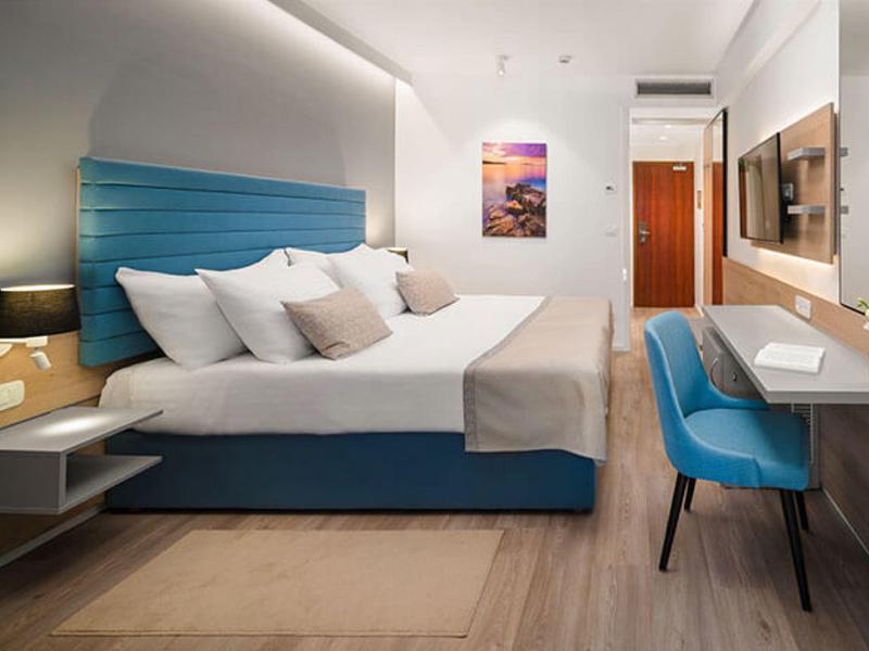 Modernes Hotelzimmer mit großem Bett, blauen Akzenten und Schreibtisch mit Stuhl.