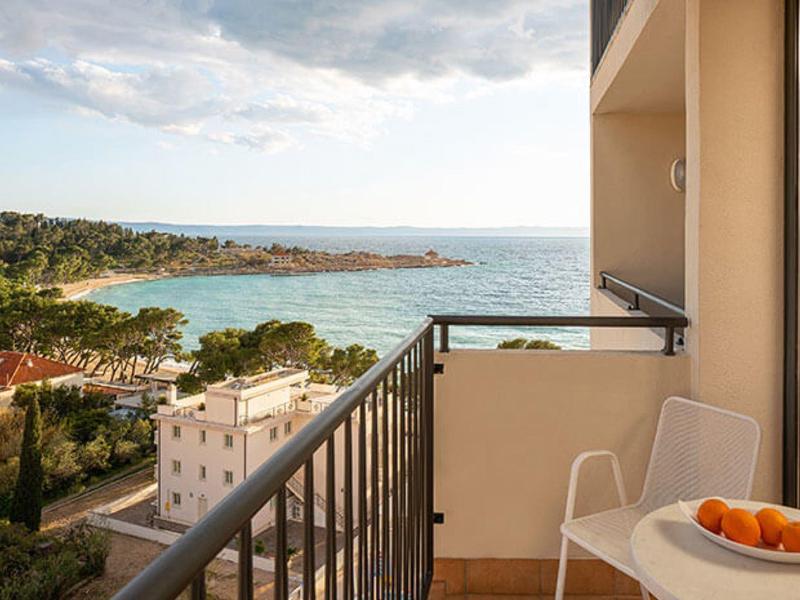 Balkon mit Blick auf das Meer, Holzstuhl, weißer Tisch mit Orangen, bewölkter Himmel.