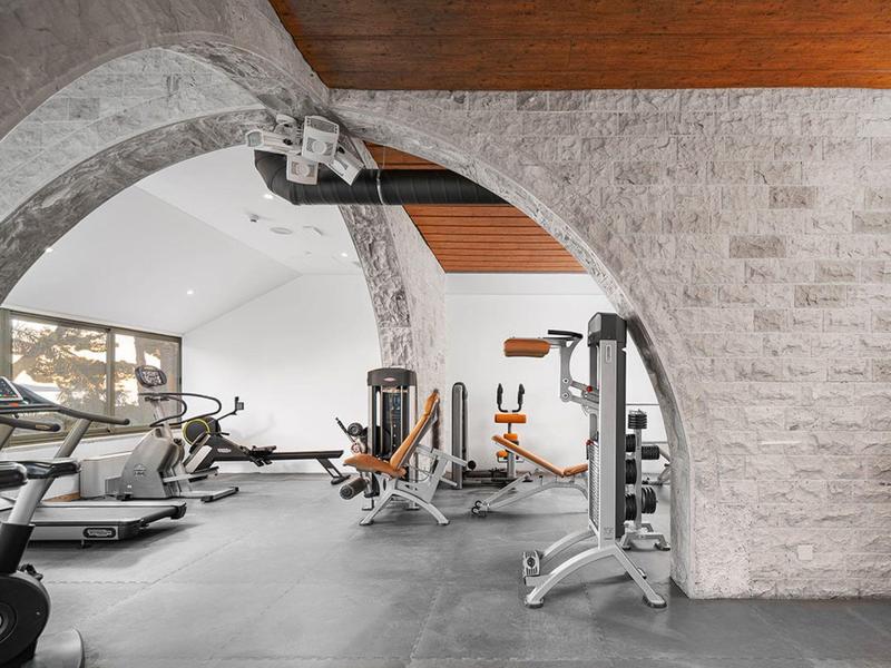 Moderner Fitnessraum mit Grauem Steinbögen, trainierenden Geräten und Holzdecke.