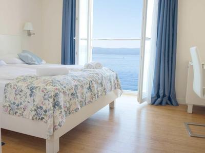 Hell eingerichtetes Hotelzimmer mit Doppelbett und Meerblick durch große Fenster.