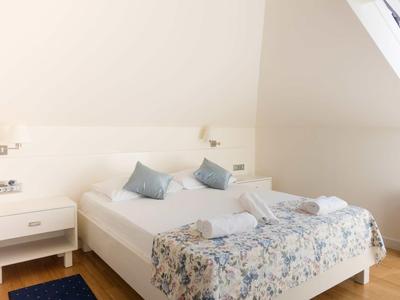 Helles Schlafzimmer mit Doppelbett, floralem Bettüberwurf und zwei Nachttischen unter einer Dachschräge.