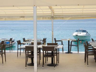 Restaurantterrasse mit Tischen und Stühlen am Wasser mit Ausblick auf Boote.