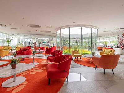 Heller Hotel-Loungebereich mit roten Sesseln, Tischen und großen Fenstern mit Blick ins Grüne.