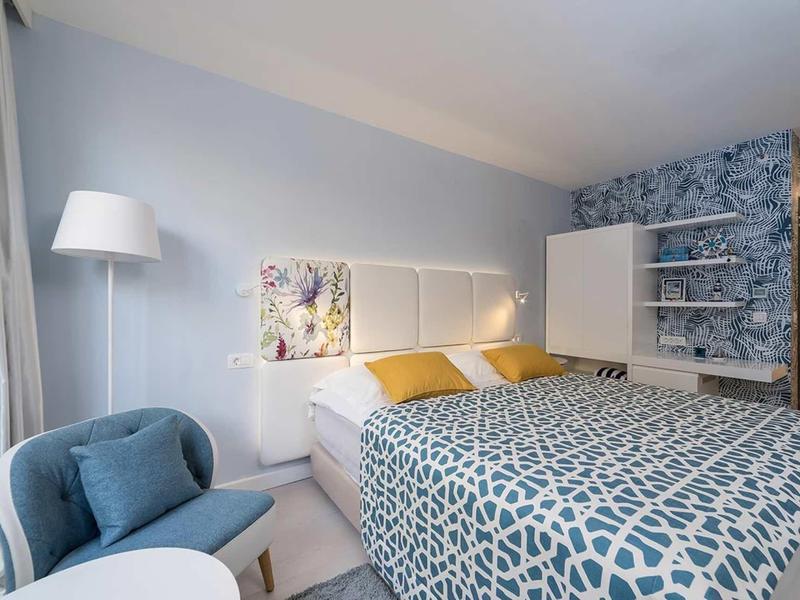 Modernes Schlafzimmer mit blauem Bett, grauem Teppich, zwei gelben Kissen und weißem Lampenständer.