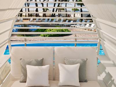 Gemütliche Outdoor-Lounge mit weißen Kissen und Blick auf einen Pool im Hotel.