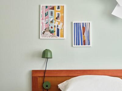 Schlafzimmer mit Holzbettrahmen, grünem Nachttischlampe und zwei Bildern über dem Bett.