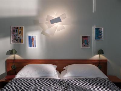 Schlafzimmer mit Doppelbett, zwei grünen Leselampen und moderner Wanddekoration über dem Kopfteil.
