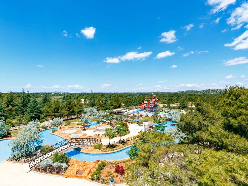 Freizeitpark mit Wasserrutschen, Pools und viel Grün unter blauem Himmel mit vereinzelten Wolken.