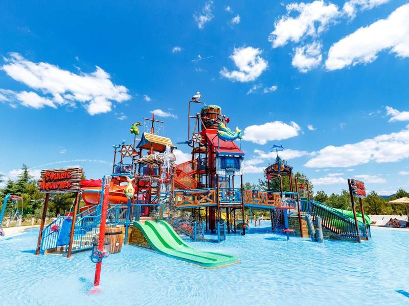 Bunter Wasserspielplatz mit Rutschen, Klettergerüsten und Wasserspielen unter blauem Himmel.