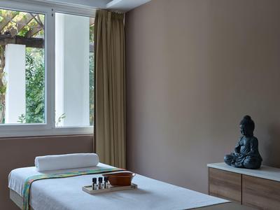Ein Wellnessraum mit Massagetisch, grünem Vorhang und Buddha-Statue auf Kommode.