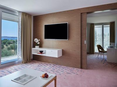 Modernes Hotelzimmer mit Fernseher an der Wand, Schreibtisch und Blick auf den Balkon mit Meerblick.