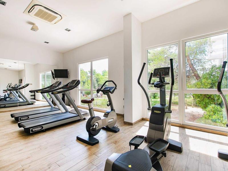 Helles Fitnessstudio mit Laufbändern, Fahrrädern, großen Fenstern und Holzboden.