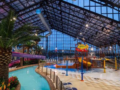 Innengelände eines tropischen Wasserparks mit Pool, Wasserrutschen und Palmen unter einem Glasdach.