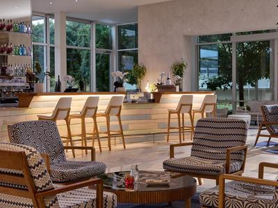Moderner Hotel-Loungebereich mit Holzstühlen, Sesseln und Blick auf grüne Umgebung.